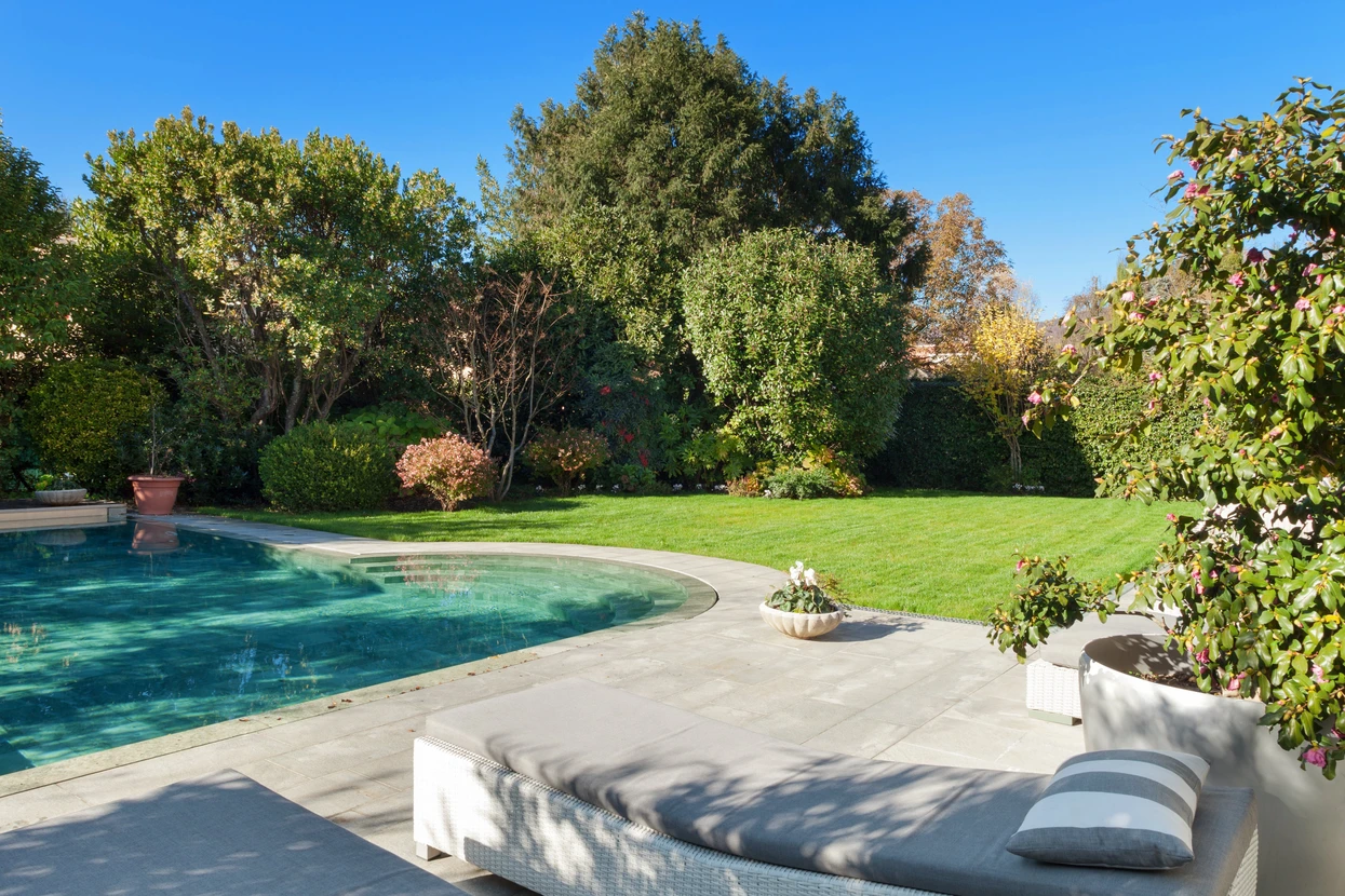 Espace extérieur résidentiel avec piscine creusée à margelles en pierre claire, terrasse dallée, transat blanc moderne