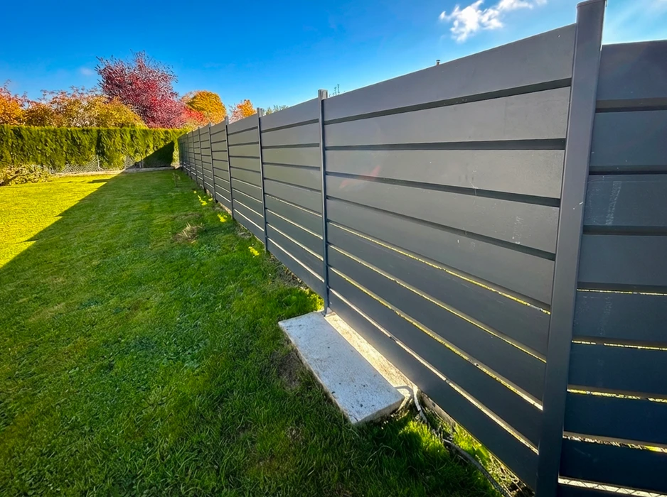 Jardin résidentiel ensoleillé en automne, clôture de séparation longeant une pelouse verte