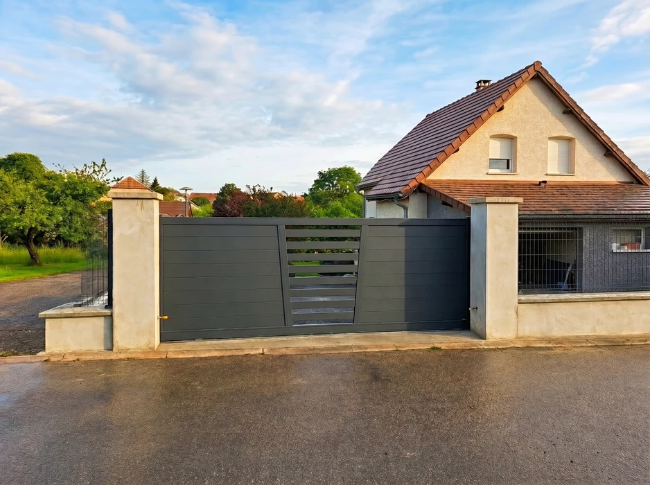 Clôture rigide en panneaux de grillage soudé anthracite (RAL 7016), avec lames brise-vue PVC ondulées horizontales, fixée sur poteaux métalliques encastrés dans un socle béton avec lit de gravier