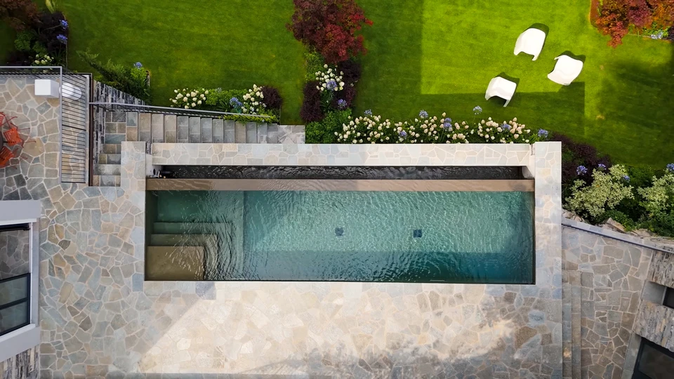 Aménagement paysager extérieur avec piscine moderne aux eaux cristallines, pelouse artificielle ou naturelle parfaitement entretenue, chemin piétonnier en dalles de pierre naturelle beige formant des courbes organiques