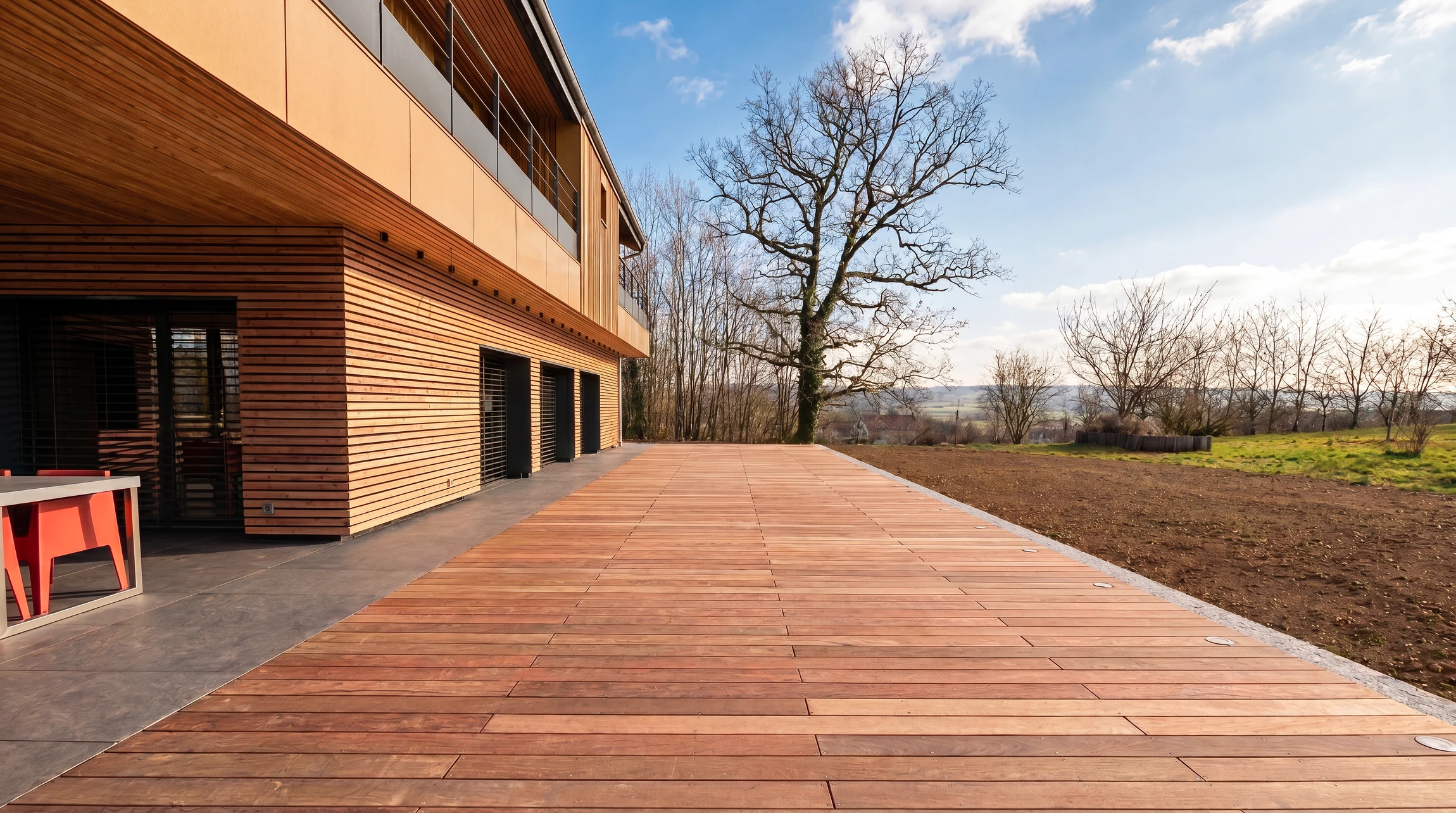 Terrasse extérieure contemporaine en bois massif, jouxtant un bâtiment à bardage bois horizontal